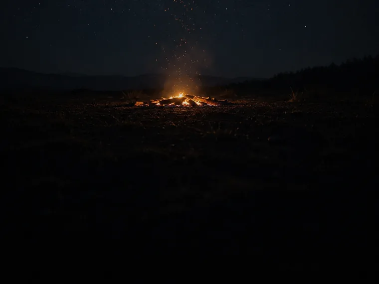 A campfire burning low under a starfield.